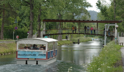 Foto: Lenkanal mit dem Boot Lendwurm, Aufdruck des Bootes geändert zu Hochschule 2026; https://upload.wikimedia.org/wikipedia/commons/7/76/Lenkanal_mit_Lendwurm_01.jpg